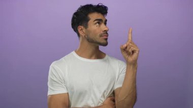 Beyaz tişörtlü bir adam işaret parmağını ciddi bakışları ve odaklanmış duruşuyla stüdyoda yukarı kaldırıyor..