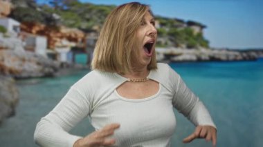 Kadın elini kaldırır ve sürpriz bir şekilde ağzını açar. Deniz kıyısındaki kayalık koyda berrak turkuaz su altında parlak gökyüzü altında. Sürpriz..