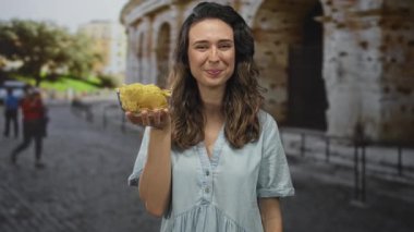 Kolezyum binasında bir kase patates kızartması tutan ve sıcak güneş ışığı altında gülümseyen bir kadın mutluluğu paylaşıyor..