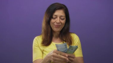 Orta yaşlı İspanyol kadın güven içinde stüdyoda mor duvara karşı Şili pesolarını sayıyor; memnuniyet.