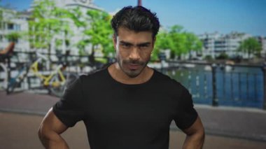 Adam şehrin ufuk çizgisinin altında silah akimbo ve sert ifade ile duruyor; kararlılık.