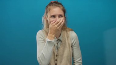 Stüdyoda gülerken elini kullanan bir kadın sarışın stili ve genç bir havanın mavi bir arkaplanı neşeli bir gülümsemeyle kapladığını gösteriyor..
