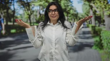 Beyaz çizgili gömlekli kadın, kırmızı tırnaklı ellerini silkiyor ve yan yan bakıyor; kafa karışıklığı şüphesi.