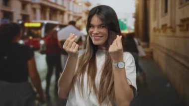 Genç İspanyol kadın gülümsüyor. Kalabalık şehir caddesinde para hareketi yapıyor. Arka planda bulanık yayalar ve binalar var..