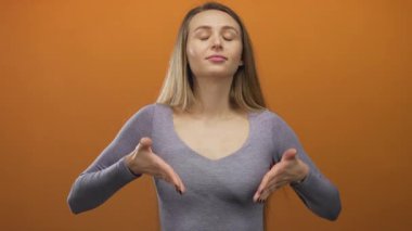 Gözleri parlak turuncu arka planda meditasyon yapan bir kadın sakin tavırlar sergiliyor ve izole bir ortamda rahatlıyor..