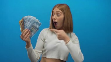 Sarı saçlı genç bir kadın mavi arka planda Macar banknotları tutuyor. Büyük gözler ve açık ağızla şaşkınlık ve haz veriyor..