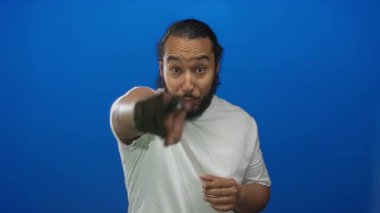 Erkekler yumruklarını sıkmış ve mavi bir stüdyoda tezahürat yapıyor, beyaz tişört ve görünür sakal giyiyor; neşeli bir kutlama..