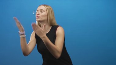 Kadın, kolsuz siyah bir tankta mavi bir stüdyo arka planına el ve dudaklarıyla bir öpücük atar; sıcak bir sevgi..