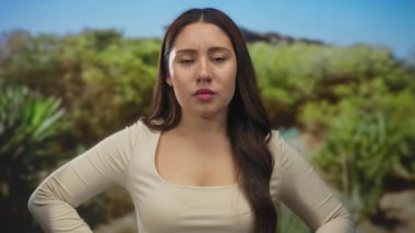 Genç İspanyol kadın, ormanda yemyeşil yeşilliklerin önünde dikilirken doğrudan kamerayı işaret ediyor. Öfke..