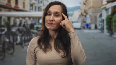 Latin kökenli genç bir kadın, park halindeki bisiklet ve dükkan cepheleriyle dolu işlek bir caddeyi işaret ediyor..