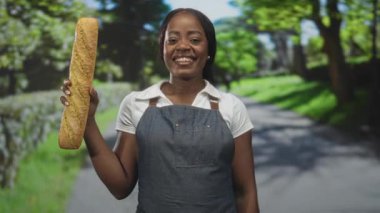 Önlüklü kadın fırıncı bir baget tutuyor ve ekmeği parmaklarıyla tadıyor, gözleri stüdyoda kapalı; zanaatkar fırın tatmini.