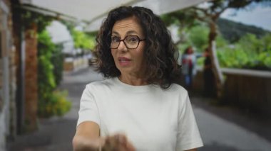 Orta yaşlı İspanyol kadın arka planda bulanık bitki ve binalarla caddeyi işaret ediyor..