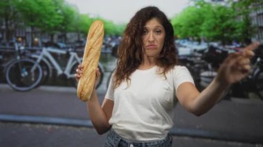 Elinde baget tutan kadın, Amsterdam caddesinde bir kanalın yanında sağı işaret ediyor ve bisikletleri park ediyor; onaylanmamış uyarı.