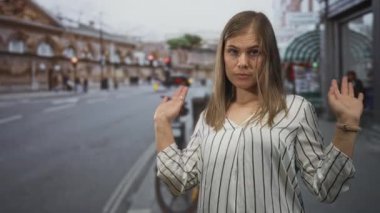 Çizgili bluzlu kadın, kaldırılmış elleri ve rüzgârlı sarı saçları olan şehir sokaklarında ince bir aldırmazlık..