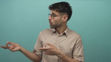 Gözlüklü ve bej tişörtlü bir adam nane atölyesine bakarken parmağıyla elini gösteriyor. Sürpriz..