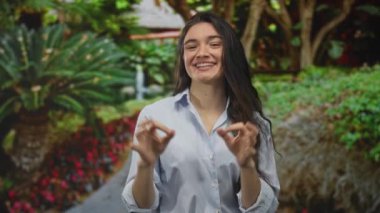 Kadın yeşil parkta elleri ile yeşil çalıların ve benekli güneş ışığı altında palmiye ağaçlarının arasına işaret koyuyor..