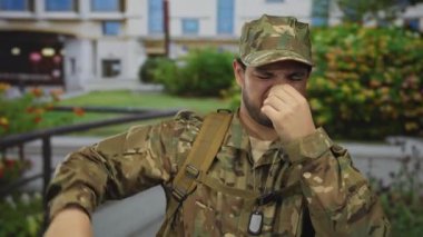 Asker, kamuflaj önlüğü üniforması ve köpek etiketiyle sokakta korkuluk yaparak burnunu çimdikliyor; iğrenme.