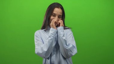 Elleriyle bir kalp oluşturan ve utangaç bir şekilde gülümseyen bir kadın, yeşil stüdyo ortamında göğsüne yakın tutulan eller; sıcak sevgi.