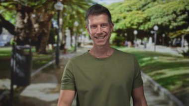 Adam, parktaki yolda el sıkışmak için gülümserken yeşillik ve güneş ışığıyla elini uzatır; dostça selamlaşır.