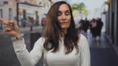 Arka planda bulanık yayalar olan bir şehir caddesinde dışarıyı gösteren bir kadın doğal ışıklandırma altında kendine güvenen bir ifade yakalıyor..