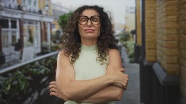 Yeşil bluzlu, kıvırcık saçlı ve gözlüklü genç İspanyol kadın caddede kollarını kavuşturuyor..