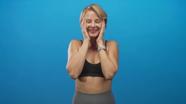 Siyah spor sutyeniyle kameraya uzanan ve stüdyoda gri taytlı bir kadın..