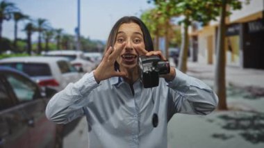 El ele tutuşan ve kalabalık bir şehir caddesinde el kamerasına bağıran genç İspanyol kadın park etmiş arabalar ve palmiye ağaçları ile eğlenceli bir heyecan.