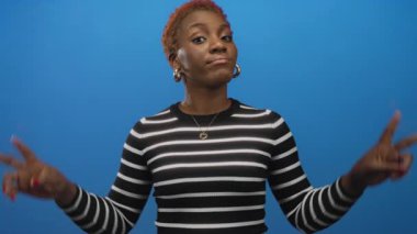 Siyah beyaz çizgili bir kadın mavi bir stüdyoda elleri havada tırnak işareti yapıyor. İğneleme şüpheciliği..