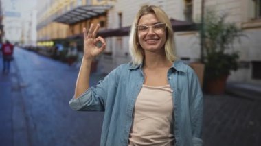 Kadın, kafelerin ve binaların önündeki kaldırım taşı caddesinde el işareti yaparken görülüyor..