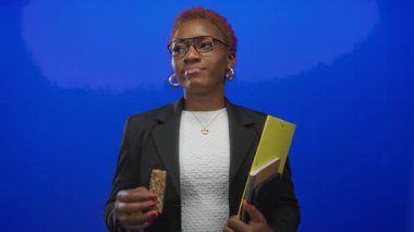 Gözlüklü genç kadın stüdyoda yan yana bakarken granola çubuğu ve sarı pano tutuyor; tefekkür.