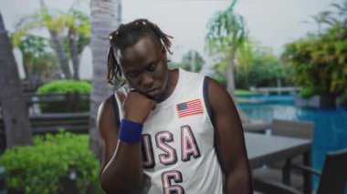 El ve çene üzerinde ABD forması giyen bir adam tatil yeri bilardo masası ve palmiye ağaçları; sessiz tefekkür.