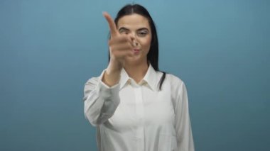 Gülümseyen ve doğrudan kameraya bakan bir kadın. Saf mavi bir duvara bakıyor. Kendine güvenen bir hareket için beyaz gömlek giyiyor..