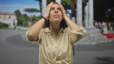 Kadın, plazada el ele tutuşuyor taş kolonlar, yukarı bakıyor bej gömlek ve saat ile; hüsran yolculuk anı.