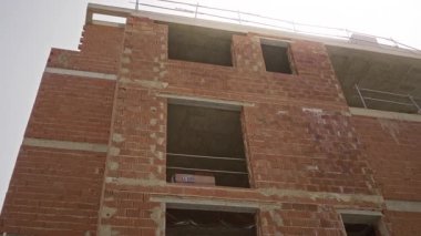 Açık pencereli cephe, istiflenmiş tuğlalar ve bir inşaat alanında etkin yapıyı gösteren metal iskeleler; tamamlanmamış geliştirme.