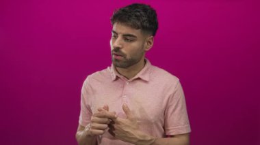 Pembe polo tişörtü giyen İspanyol genç adam pembe bir stüdyoda parmaklarını birbirine değdiriyor..