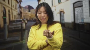 Caddedeki sarı süveter içinde yüzüğe dokunan kadın parmakları görünür, düşünceli iç gözlem..