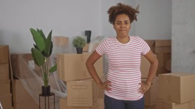 Karton kutular arasında kolları çapraz duran bir kadın ve bir bina odasında saksı bitkisi açılırken; kendine güven yeni bir başlangıç.