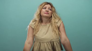 Sarışın genç bir kadın stüdyoda bej renkli kolsuz bir bluz giyen ve yukarı bakıyor, kendini rahat hissetme hassasiyeti var..