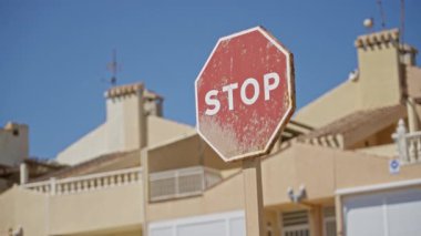 Güneşli bir günde açık mavi gökyüzü ve arka planda güneş tarafından öpülen bej binalara karşı dur işareti..