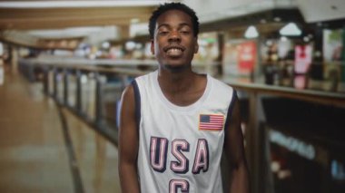 Amerikan bayraklı beyaz Amerikan basketbol forması giyen bir adam binadaki gülümseyen yüzüyle yumruk atıyor..