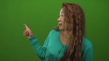 Deniz mavisi süveter giyen genç bir kadın, parmaklarını çıplak elle gösteriyor ve stüdyo yeşil ekranında omuz silkiyor..