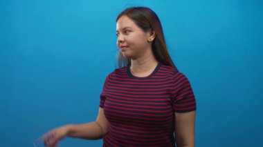 Stüdyoda sessizlik için parmakları dudaklarına kadar uzanan kırmızı ve lacivert çizgili gömlek giyen ve mavi duvara karşı el ele tutuşan bir kadın..