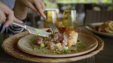 Lokanta masasında elleriyle deniz ürünleri yemekten hoşlanan bir kadın, canlı ve taze bir yemek sunumu sunuyor çatal bıçak takımı ve modern yemek takımı ile.
