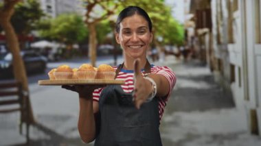 Genç İspanyol kadın elinde ahşap kek tepsisi ve sokakta el sıkışmak için uzatan el sıkışma; dostça karşılama.