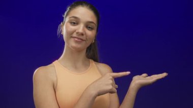 Kafkasyalı genç kız açık avuç gösteriyor ve stüdyoda mavi arka planda eli işaret ediyor; neşe.