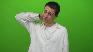 Beyaz gömlekli bir adam yeşil stüdyoda boynu için gergin duruş ve eli ile boyun bastırıyor; rahatsızlık.