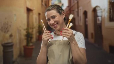 Elinde fırça tutan ve gülümseyen bir kadın tarihi binalarla dolu güneşli eski bir kasaba caddesinde..