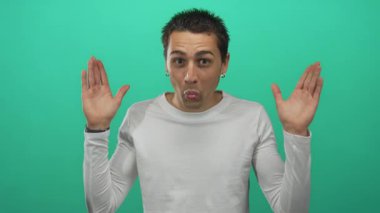 Beyaz tişörtlü genç adam elleri ile gözlerini kapar sonra stüdyoda ellerini indirir ve gülümser; neşeli bir neşe.