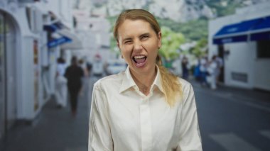 Kadın neşeli bir şekilde şehir sokaklarında dilini uzatıyor, gençlik enerjisi ve günlük moda sergiliyor şehir manzarasının ortasında beyaz bir gömlekle..