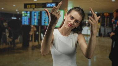 Kadın, havaalanı terminalinde kontrol monitörlerinin yanında çıplak kollarıyla orta parmaklarını kameraya doğru kaldırıyor..